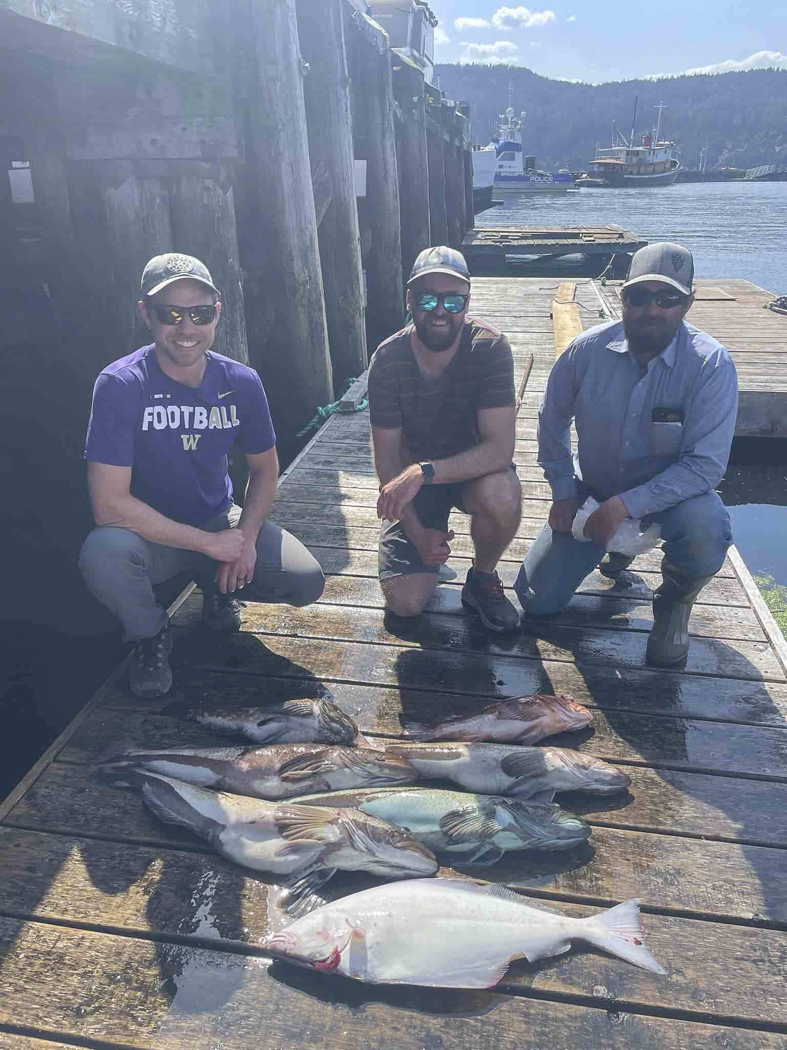 a group of men posing for a picture with fish on a dock