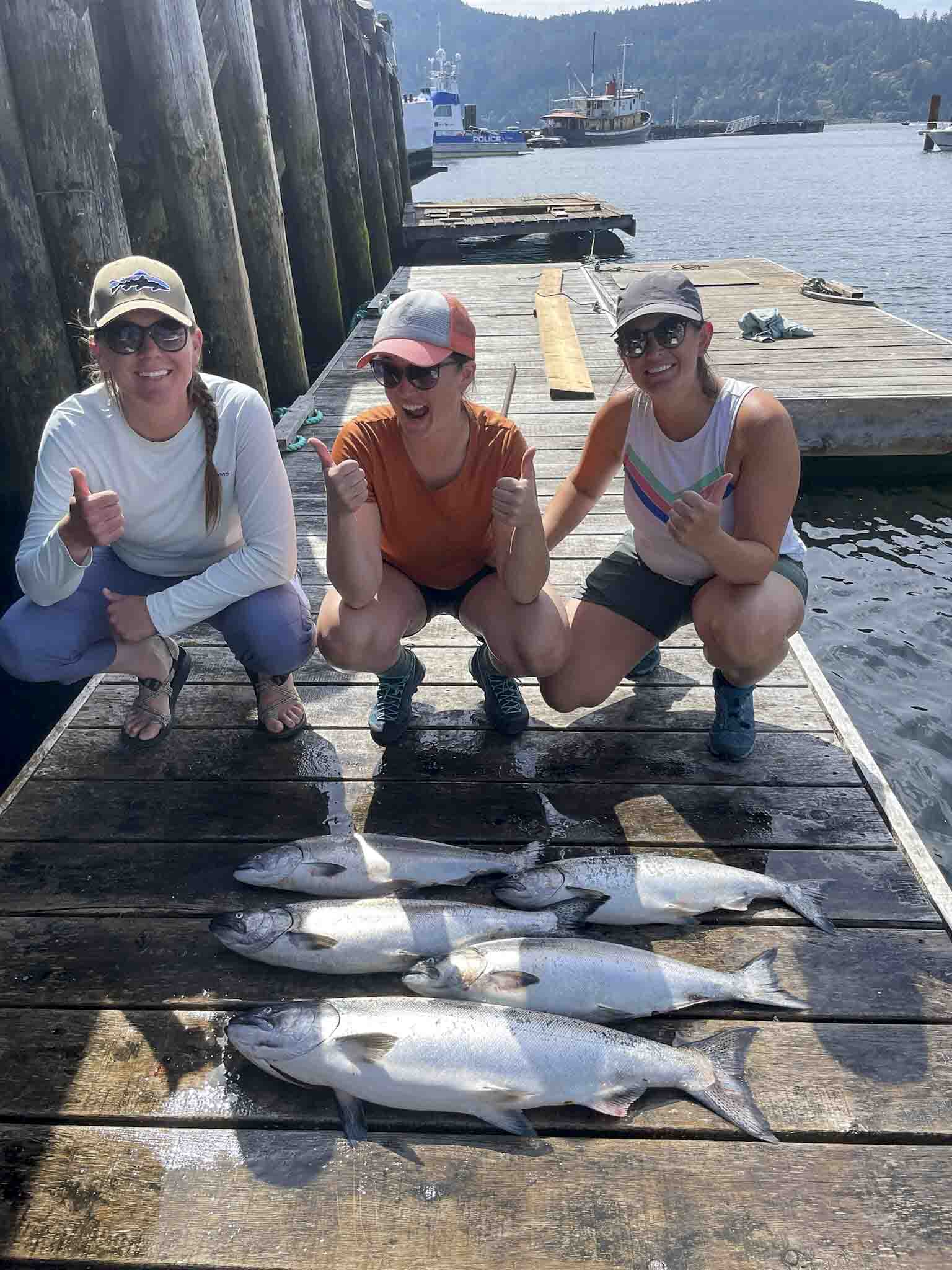 a group of women posing with fish on a dock